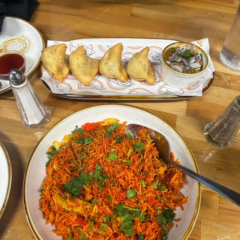 A wooden table with a plate of samosas, a bowl of biryani, and condiments.