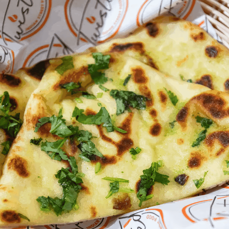 Golden naan bread, garnished with fresh cilantro, served in a woven basket lined with branded paper.
